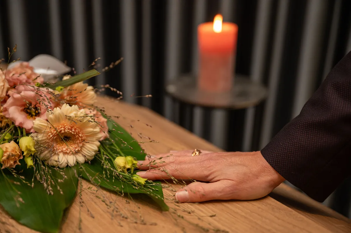 Hand rust op een houten kist met bloemen, met een brandende kaars op de achtergrond