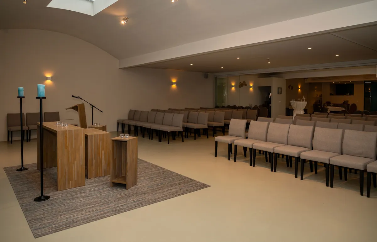 Aula van Uitvaartcentrum Melis met houten spreekgestoelte, kaarsen en rijen stoelen